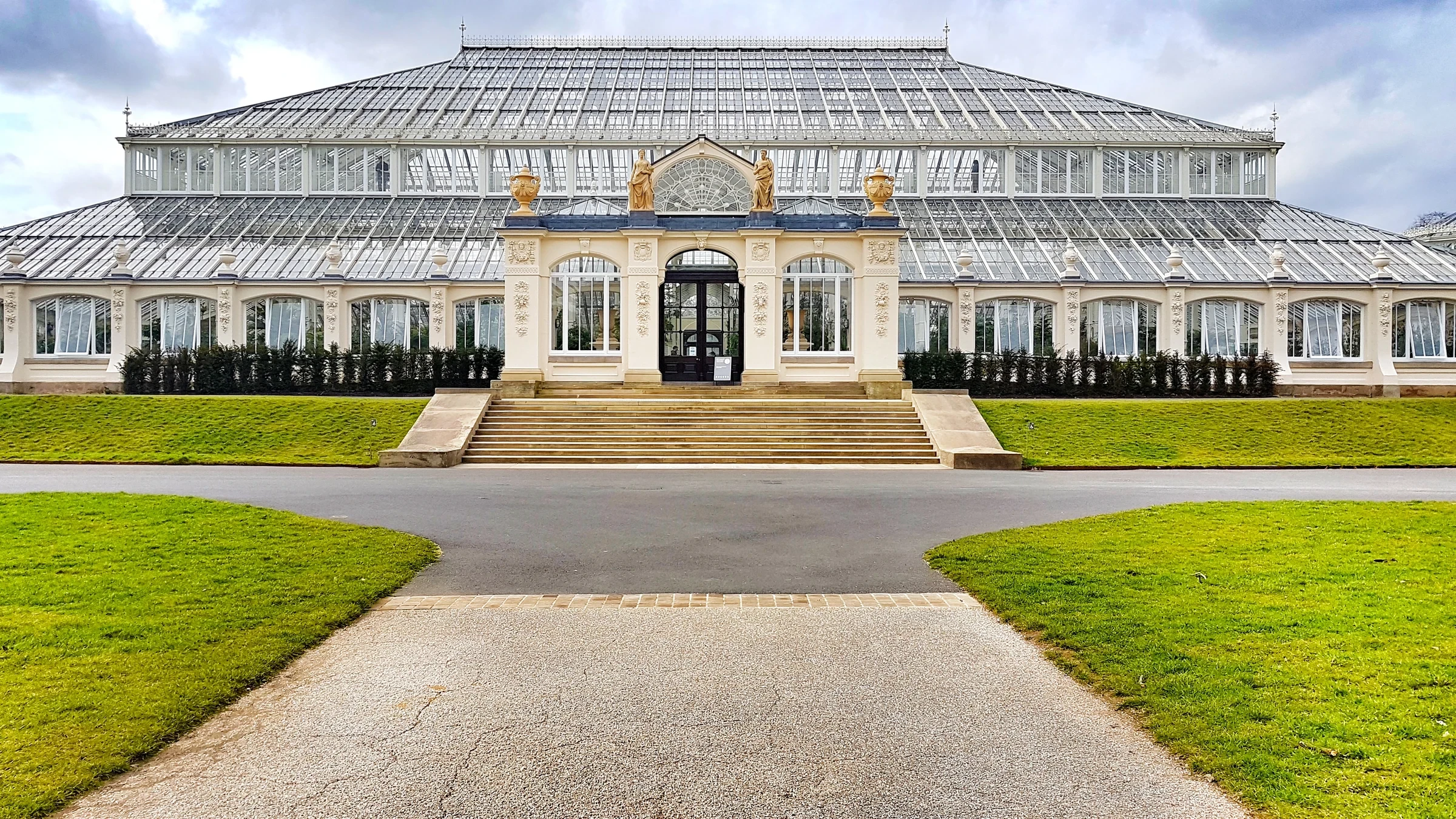 The white façade and central glass roof of the Temperate House at Kew Gardens, seen across its lawn.