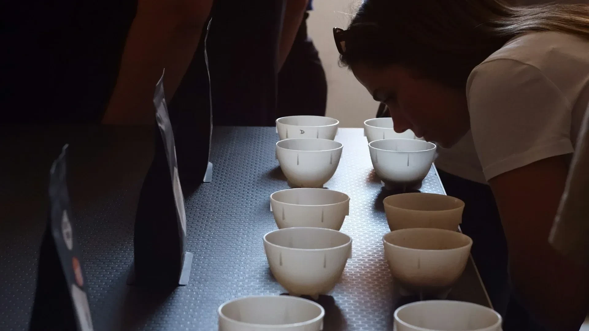 Een deelnemer buigt naar een witte kom om een koffiemonster te ruiken, naast een rij proefkommen.