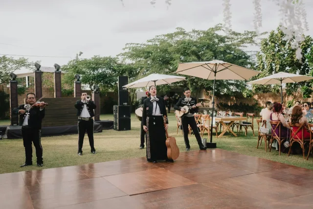 Mariachi singer, violinist, trumpeter and guitarists performing beside seated guests at an outdoor wedding reception