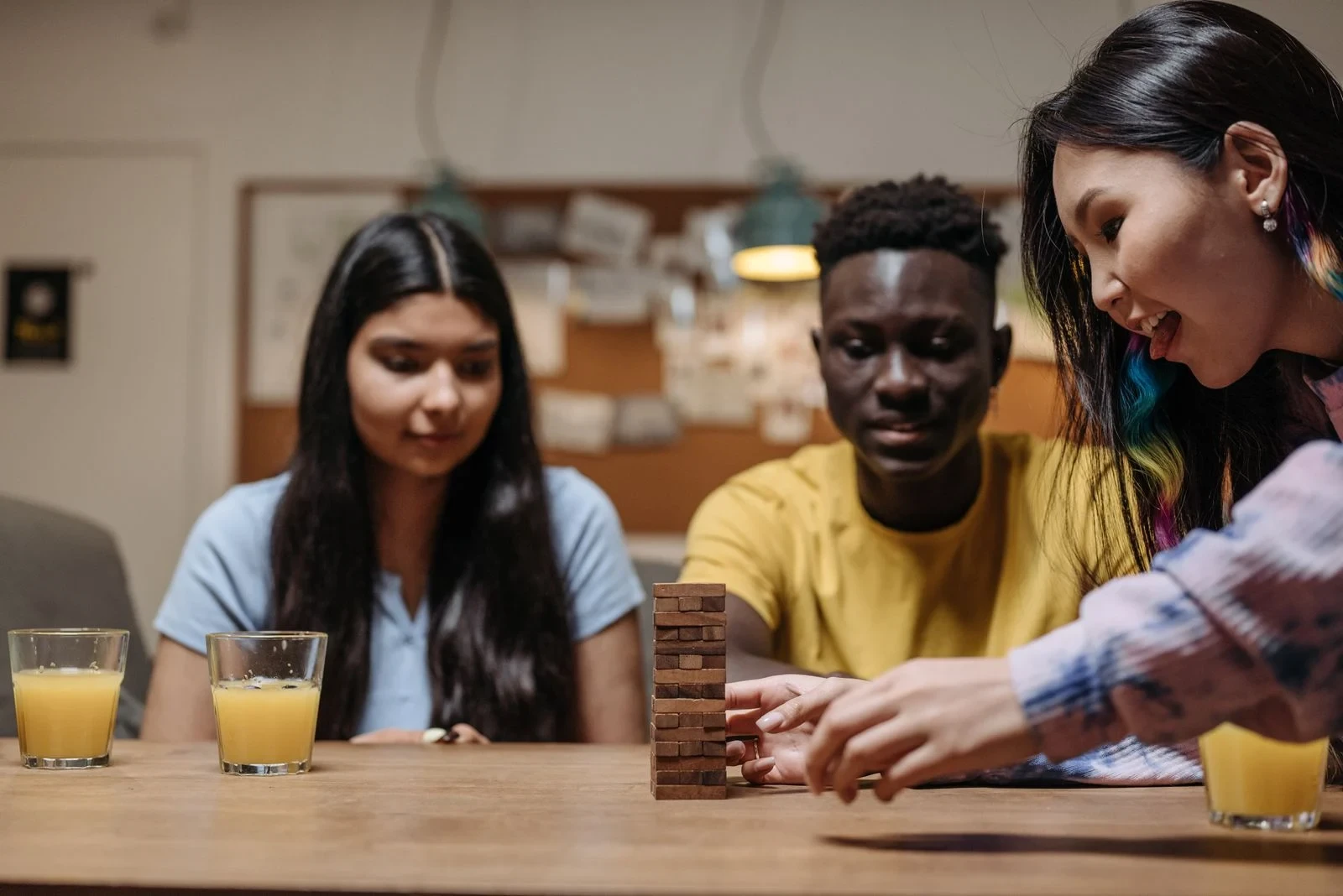 Trois personnes autour d’une table, dont une retire délicatement un bloc d’une tour en bois.