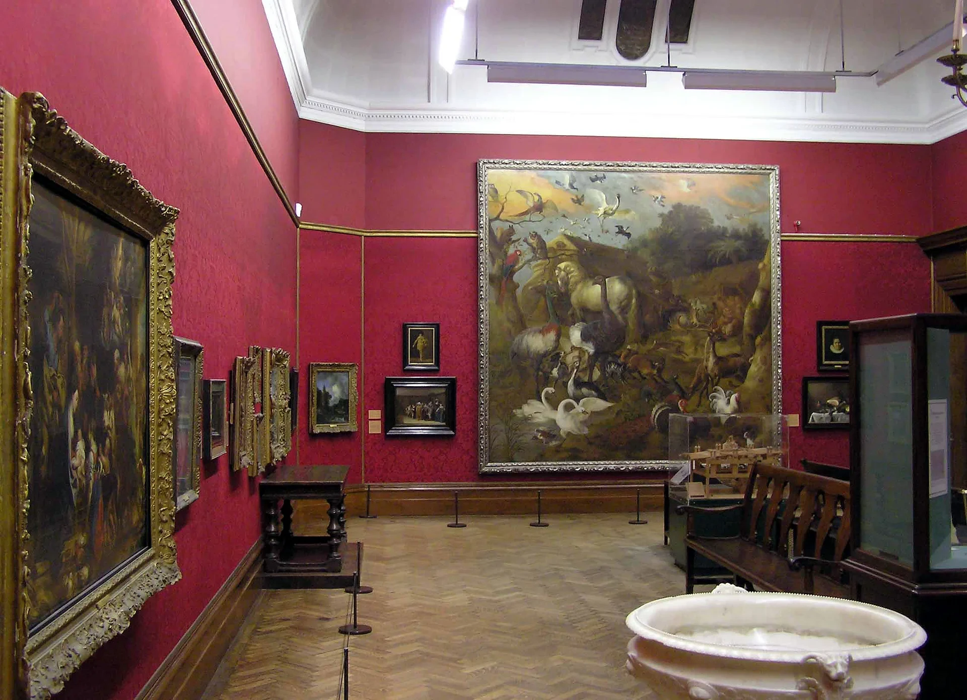 Paintings displayed on red walls inside Bristol Museum & Art Gallery.