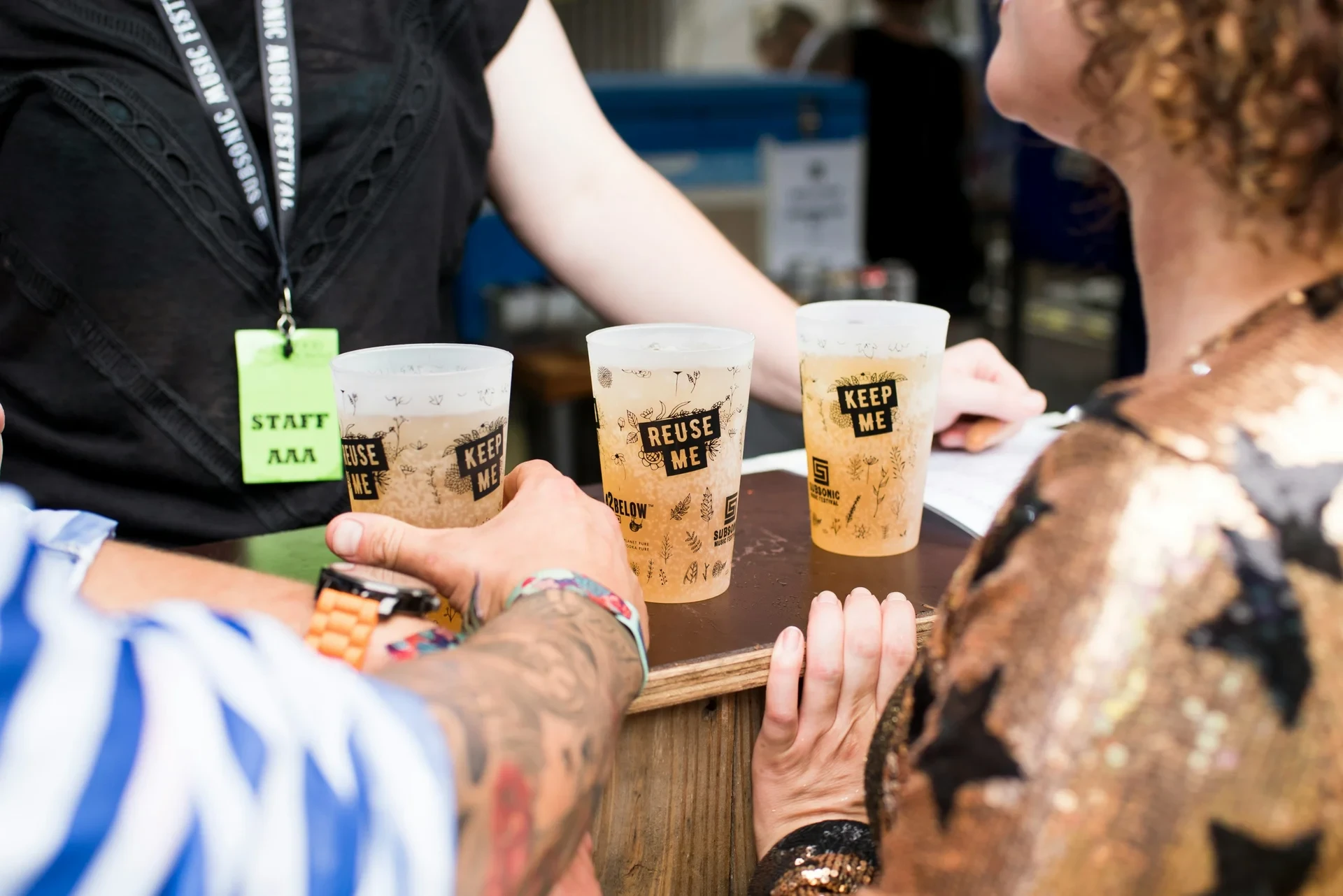 Three reusable drinks cups marked Reuse Me and Keep Me on a festival bar counter
