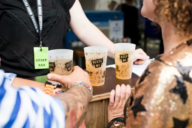Three reusable drinks cups marked Reuse Me and Keep Me on a festival bar counter