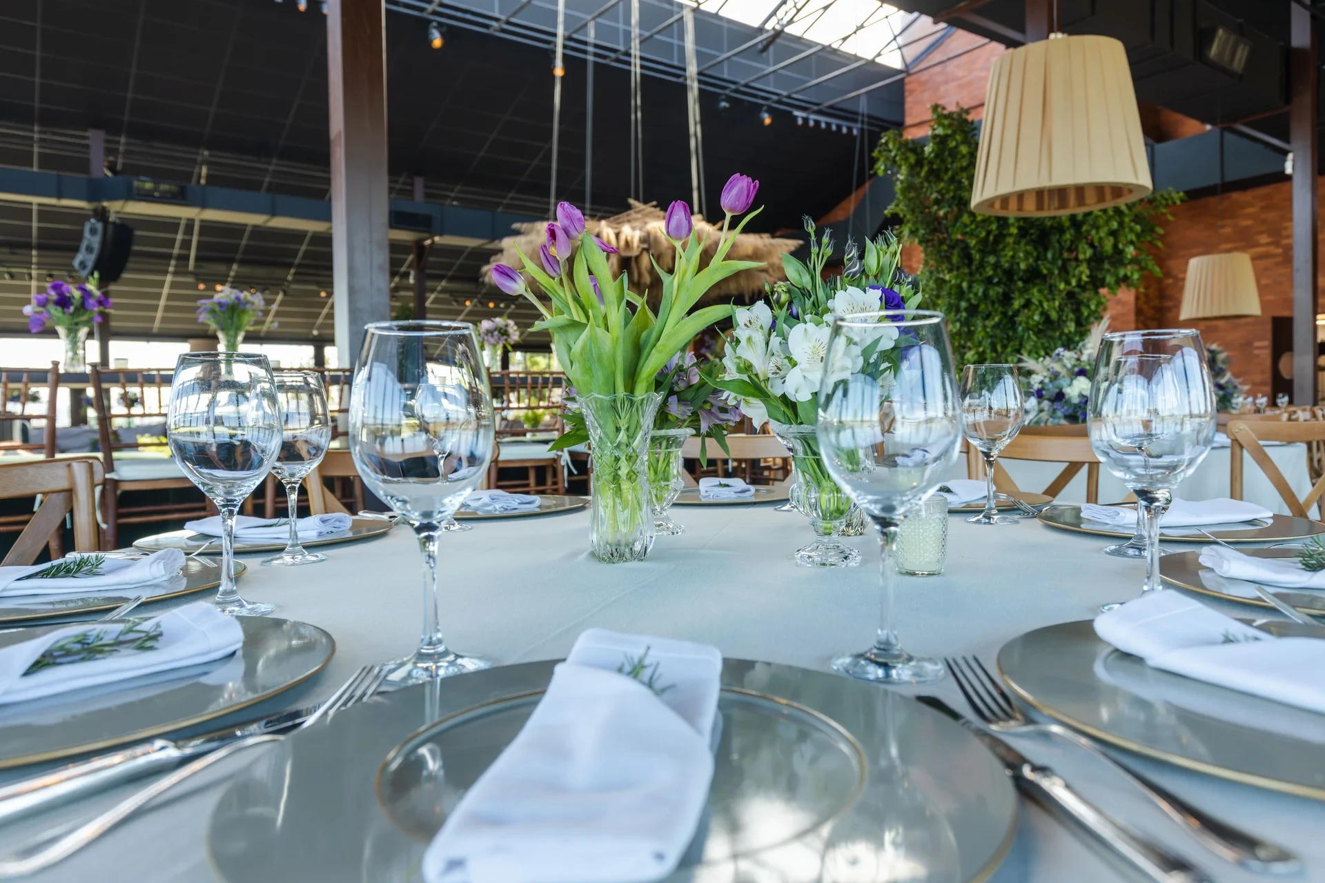 Purple and white cut flowers in clear glass vases on a reception table set with glasses and plates.