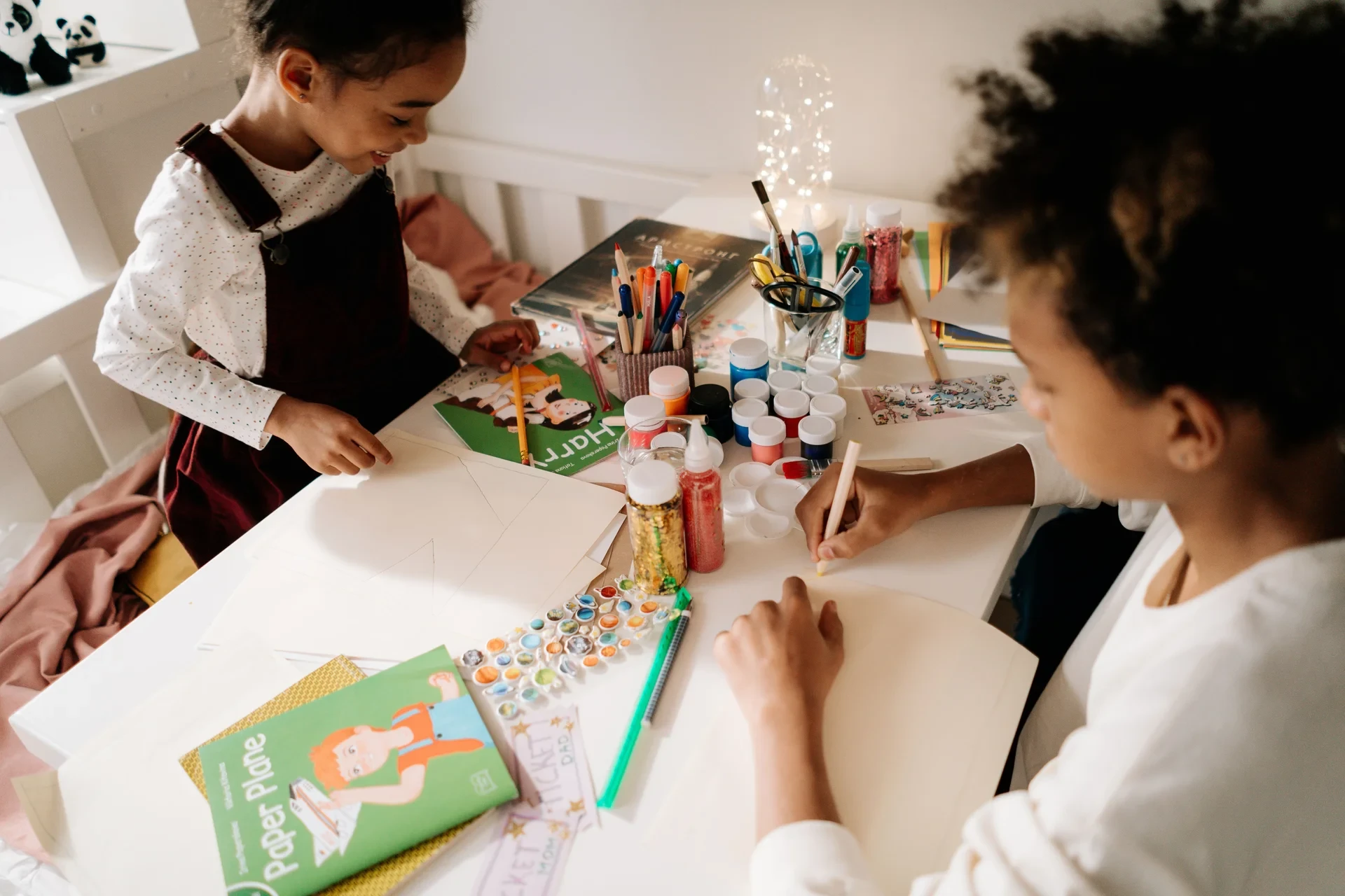 Two children draw and work with paper, markers and craft materials at a table.