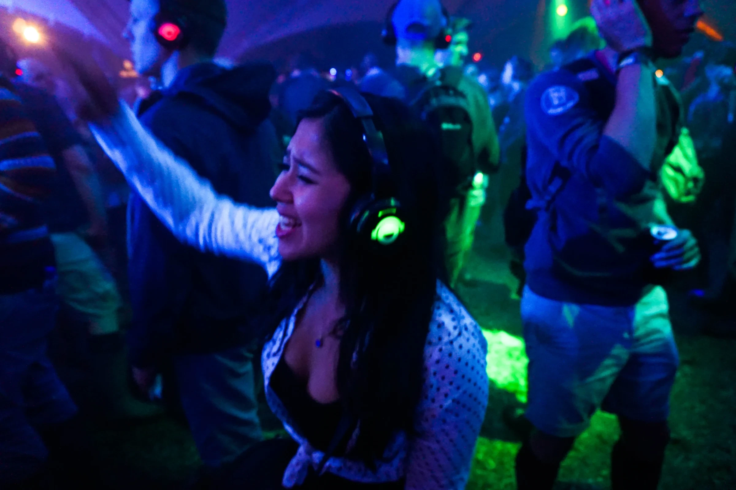 Een festivalbezoekster danst met één arm omhoog tussen mensen met hoofdtelefoons die in verschillende kleuren oplichten.